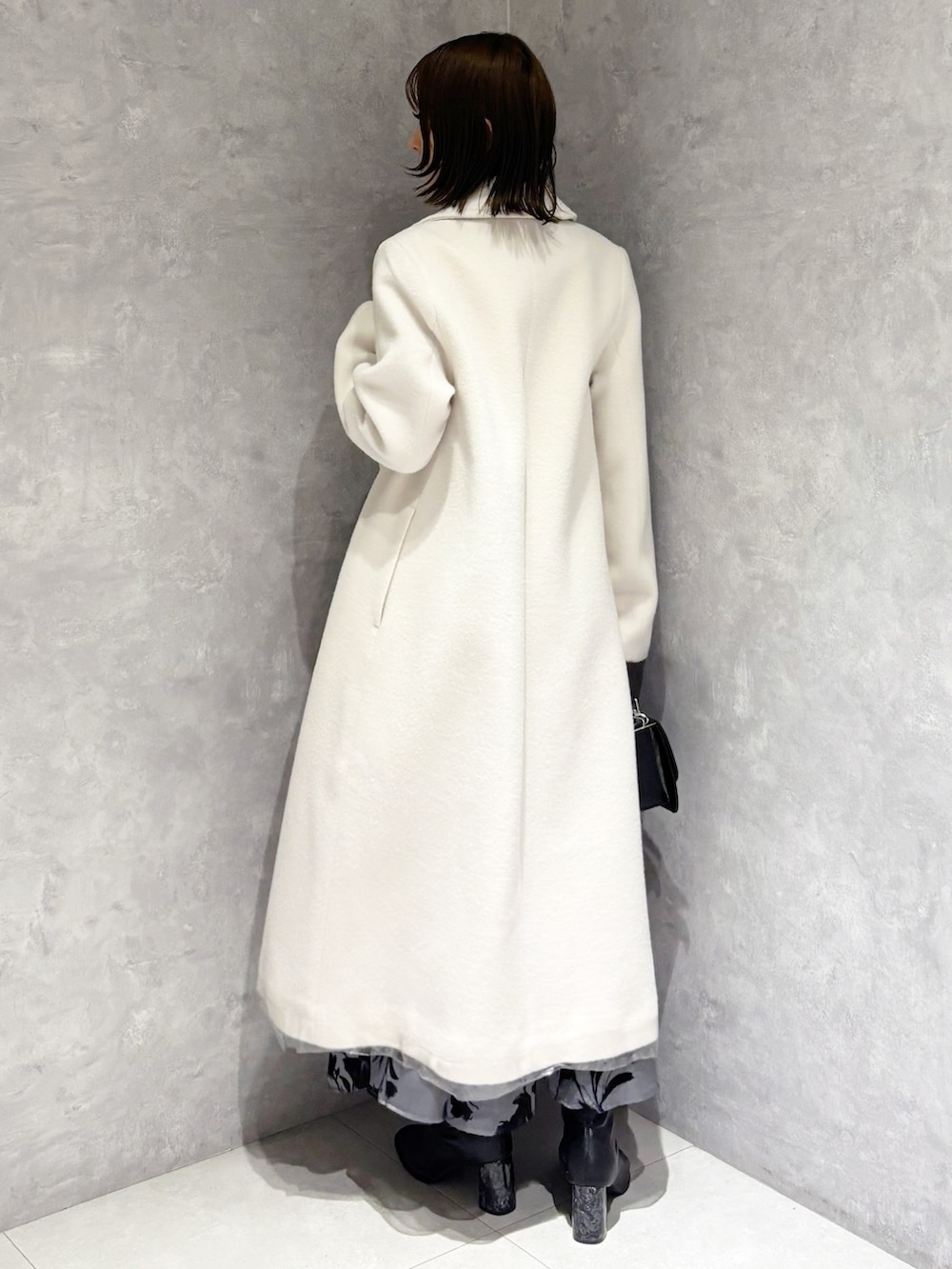 ホワイト系のチェスターコート、ブラック系のブーツ、ホワイト系のニット/セーターを着用したレディースの冬コーディネートの3枚目の写真