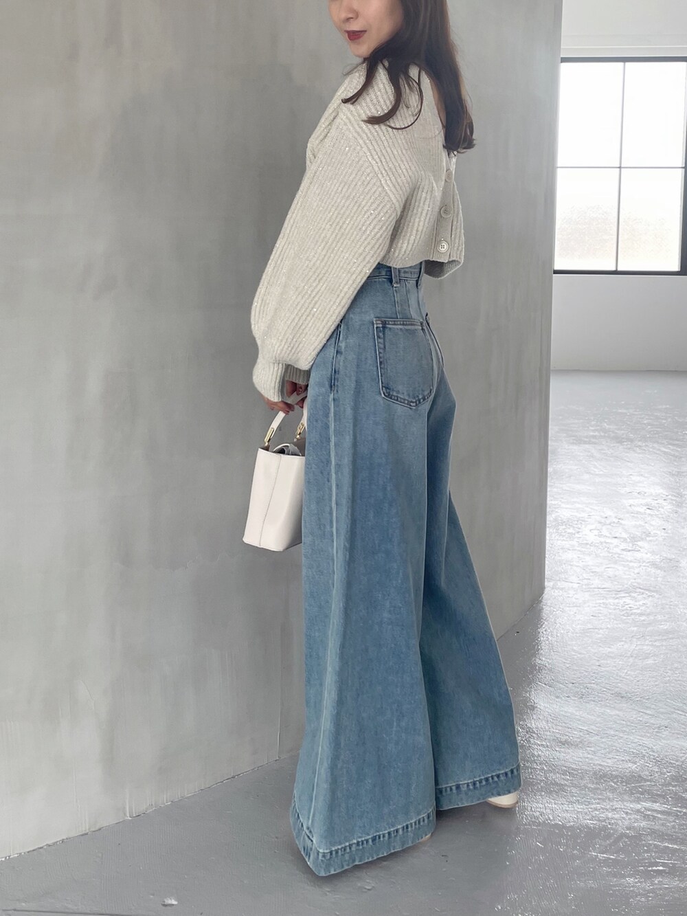 ホワイト系のブーツ、ホワイト系のハンドバッグ、ブルー系のデニムパンツを着用したレディースの秋コーディネートの2枚目の写真