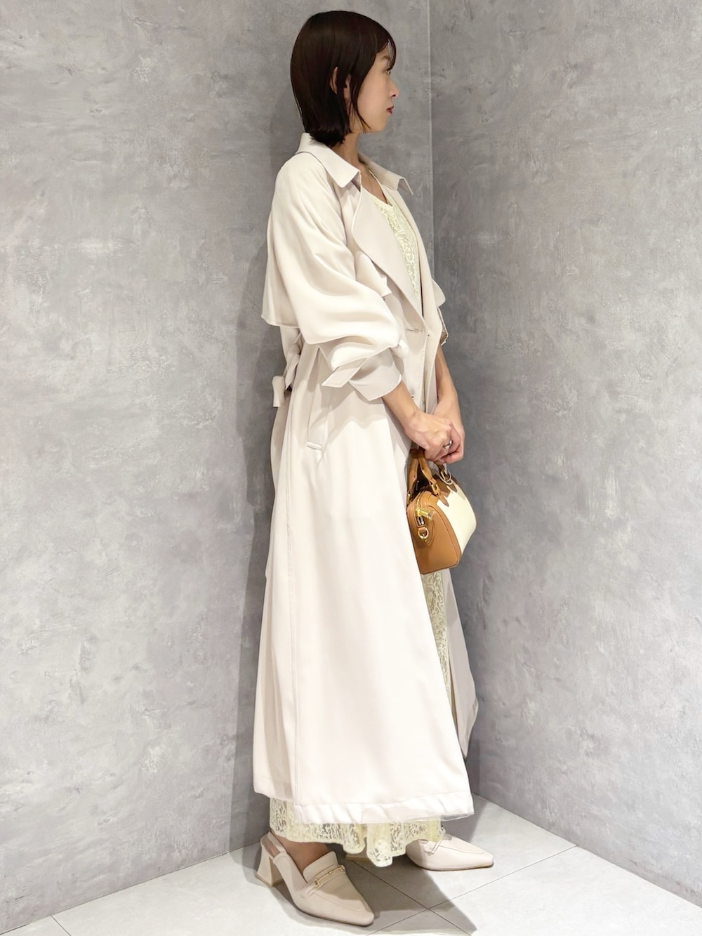 イエロー系のワンピース、ホワイト系のパンプス、ブラウン系のハンドバッグを着用したレディースの春コーディネートの2枚目の写真