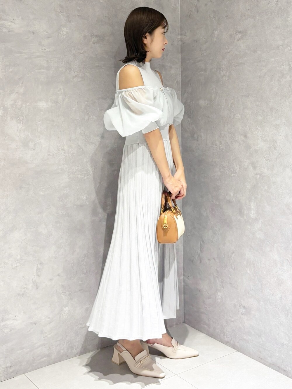 グレー系のワンピース、ホワイト系のパンプス、ブラウン系のハンドバッグを着用したレディースの春コーディネートの2枚目の写真