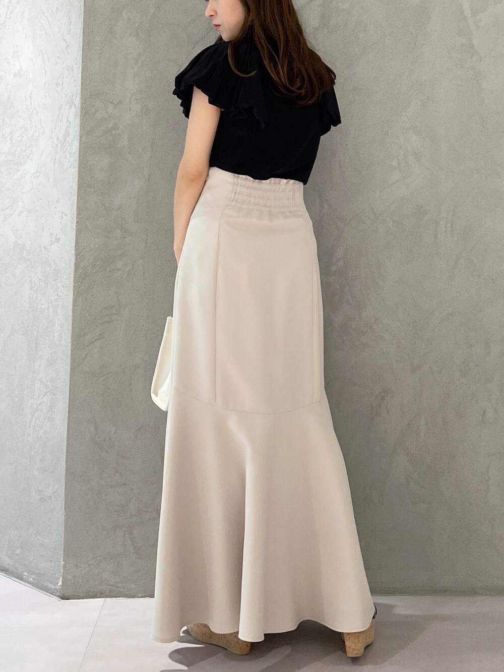 グレー系のハンドバッグ、ベージュ系のスカート、ブラック系のサンダルを着用したレディースの春コーディネートの3枚目の写真