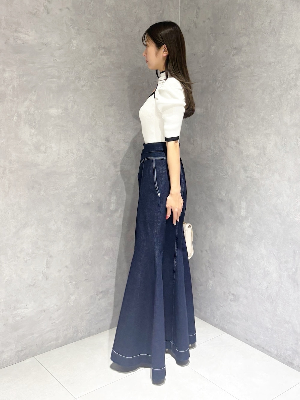 ブルー系のスカート、ホワイト系のパンプス、ホワイト系のハンドバッグを着用したレディースの春コーディネートの2枚目の写真