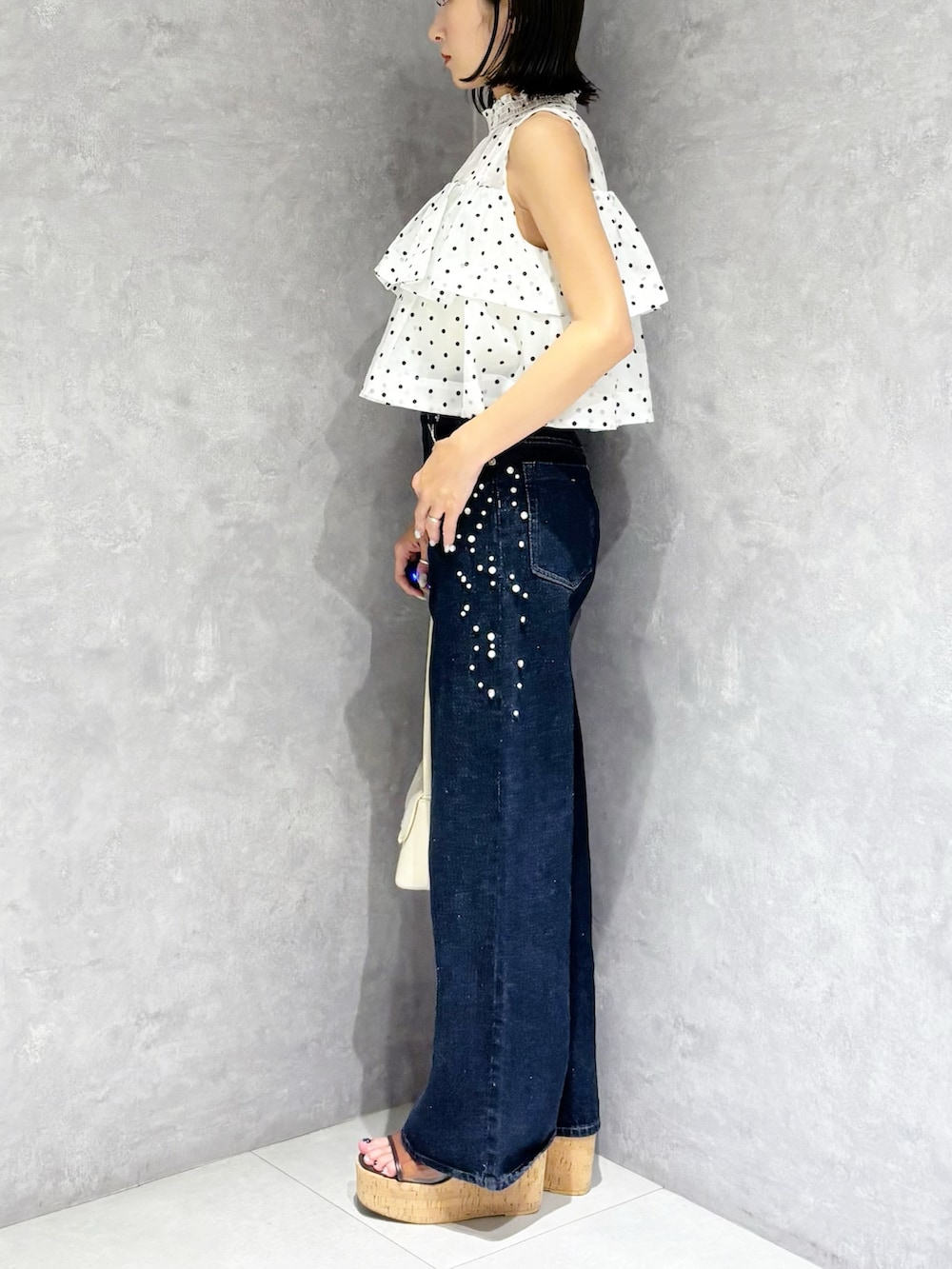 ブルー系のデニムパンツ、ブラウン系のサンダル、ホワイト系のハンドバッグを着用したレディースの夏コーディネートの5枚目の写真