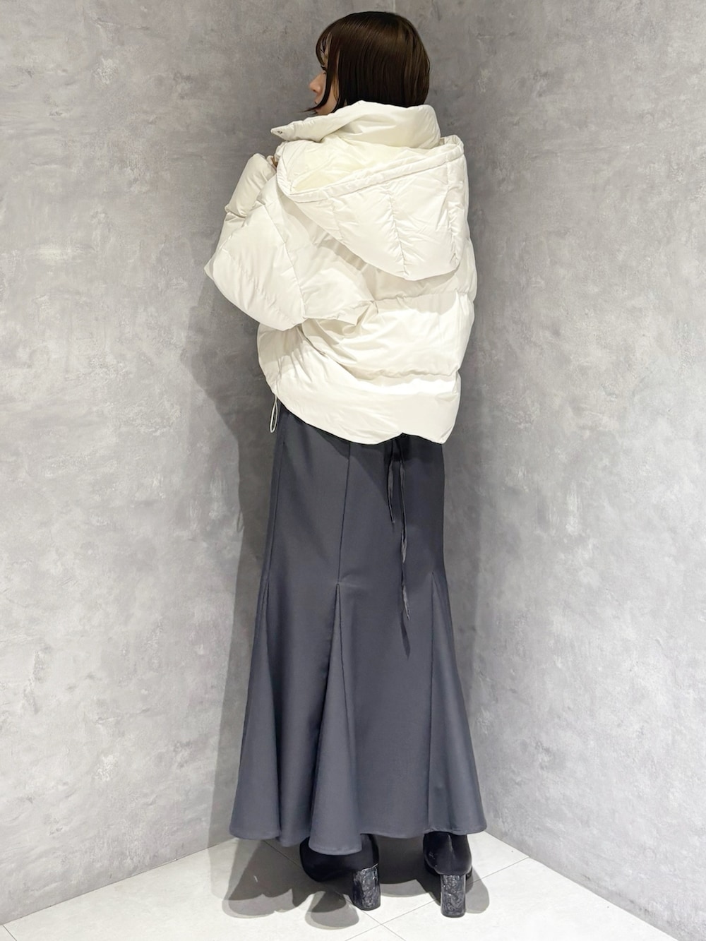 グレー系のスカート、グレー系のニット/セーター、ホワイト系のダウンジャケット/コートを着用したレディースの冬コーディネートの2枚目の写真