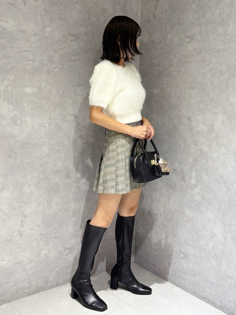 グレー系のスカート、ホワイト系のニット/セーター、ブラック系のブーツを着用したレディースの夏コーディネートの2枚目の写真