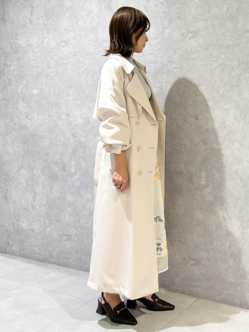 グリーン系のワンピース、ホワイト系のトレンチコート、ブラウン系のパンプスを着用したレディースの春コーディネートの3枚目の写真