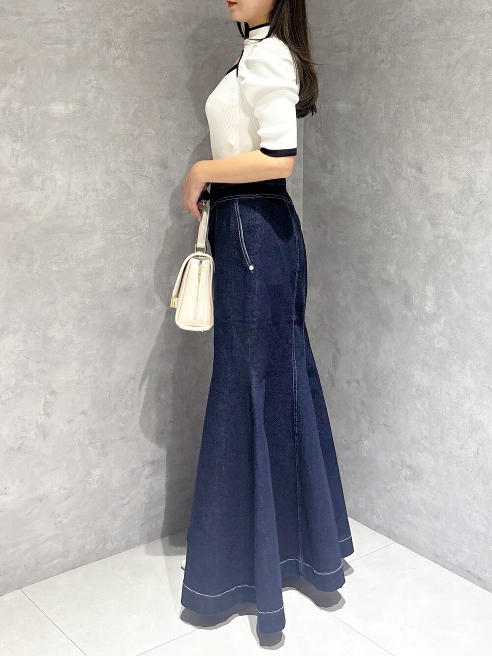 ブルー系のスカート、ホワイト系のパンプス、ホワイト系のハンドバッグを着用したレディースの春コーディネートの7枚目の写真