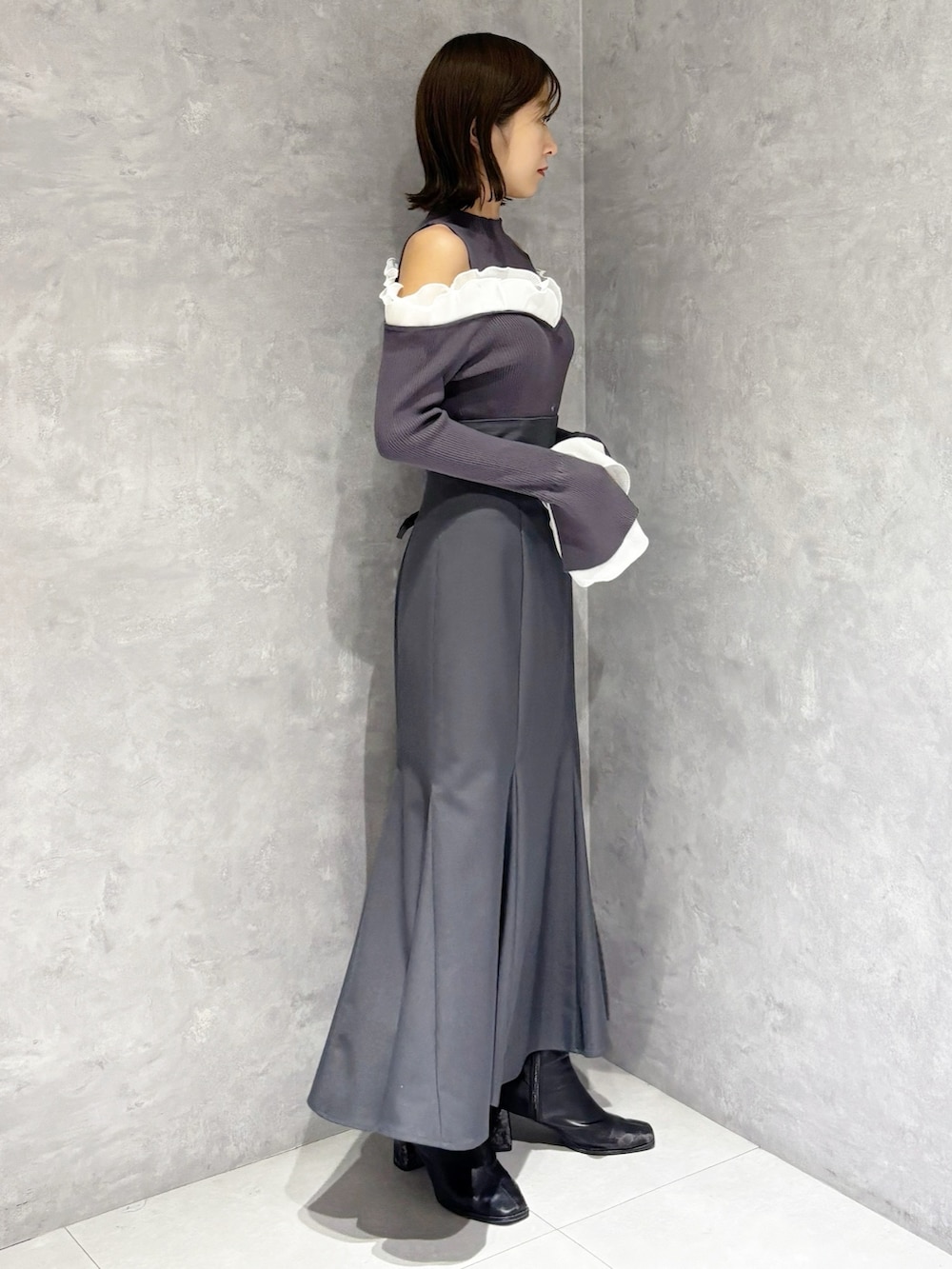 グレー系のスカート、グレー系のニット/セーター、ブラック系のブーツを着用したレディースの冬コーディネートの2枚目の写真