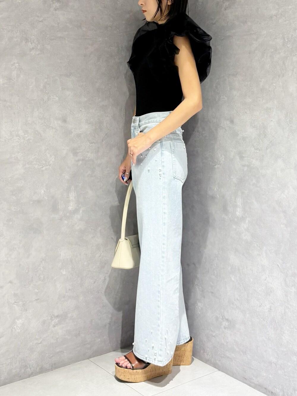 ブルー系のデニムパンツ、ブラック系のニット/セーター、ホワイト系のハンドバッグを着用したレディースの春コーディネートの5枚目の写真