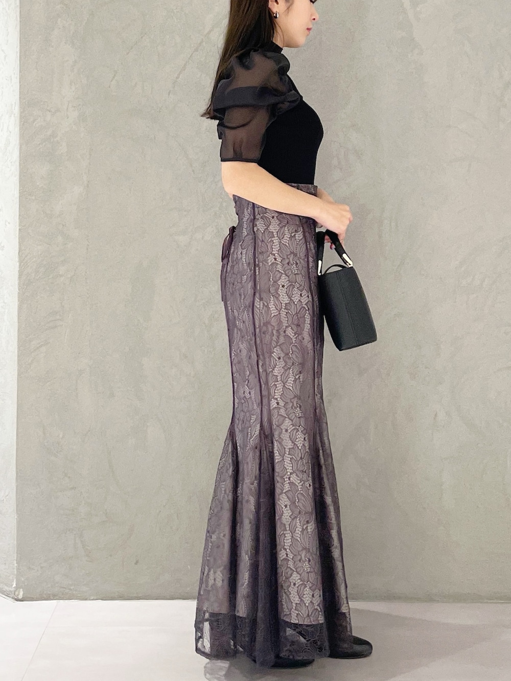 パープル系のスカート、ブラック系のハンドバッグ、ブラック系のニット/セーターを着用したレディースの春コーディネートの4枚目の写真