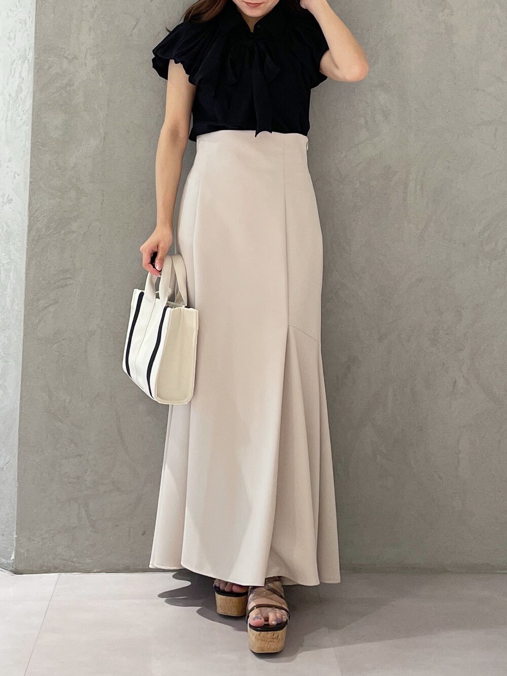 グレー系のハンドバッグ、ベージュ系のスカート、ブラック系のサンダルを着用したレディースの春コーディネートの7枚目の写真