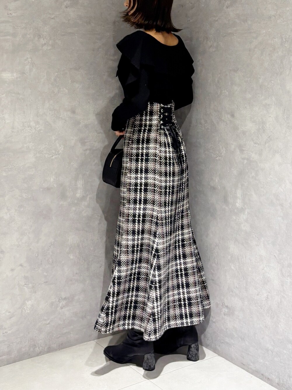 ブラック系のスカート、ブラック系のブーツ、ブラック系のハンドバッグを着用したレディースの秋コーディネートの3枚目の写真