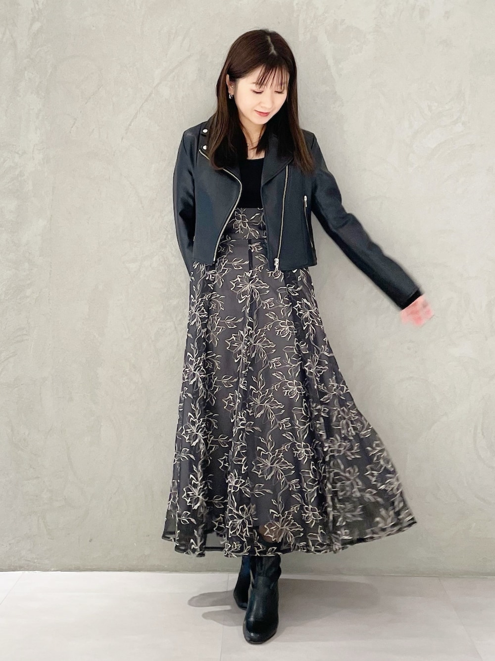 グレー系のスカート、ブラック系のライダースジャケット、ブラック系のブーツを着用したレディースの冬コーディネートの2枚目の写真