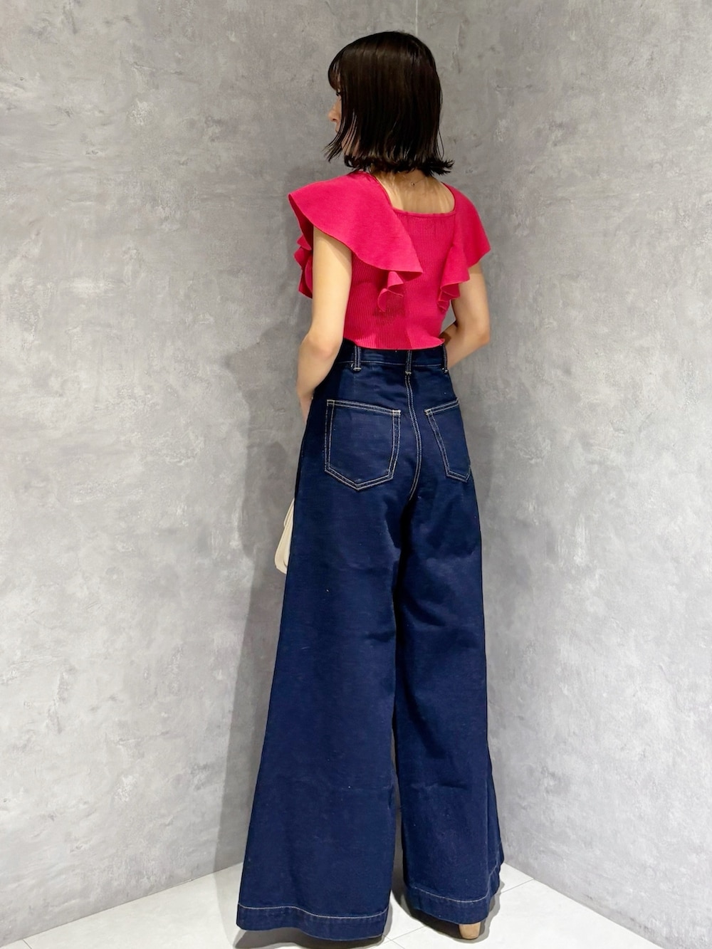 ブルー系のデニムパンツ、ブラウン系のサンダル、ホワイト系のハンドバッグを着用したレディースの夏コーディネートの2枚目の写真