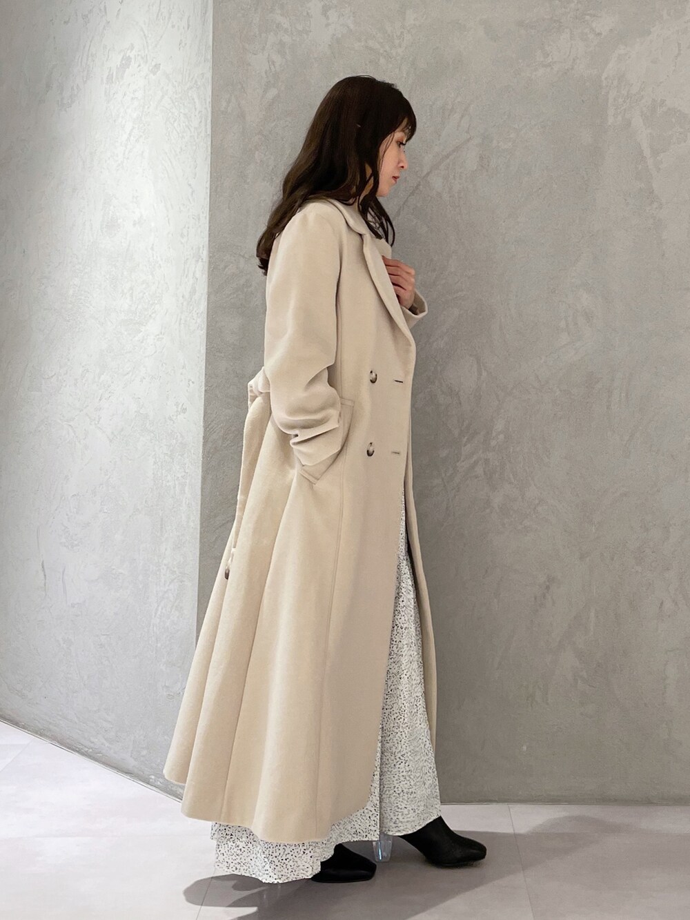 ホワイト系のワンピース、ベージュ系のチェスターコート、ブラック系のブーツを着用したレディースの秋コーディネートの2枚目の写真