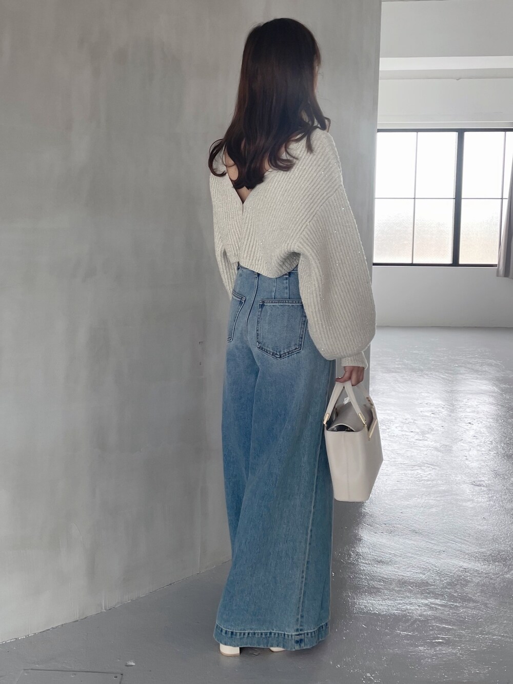 ホワイト系のブーツ、ホワイト系のハンドバッグ、ブルー系のデニムパンツを着用したレディースの秋コーディネートの3枚目の写真