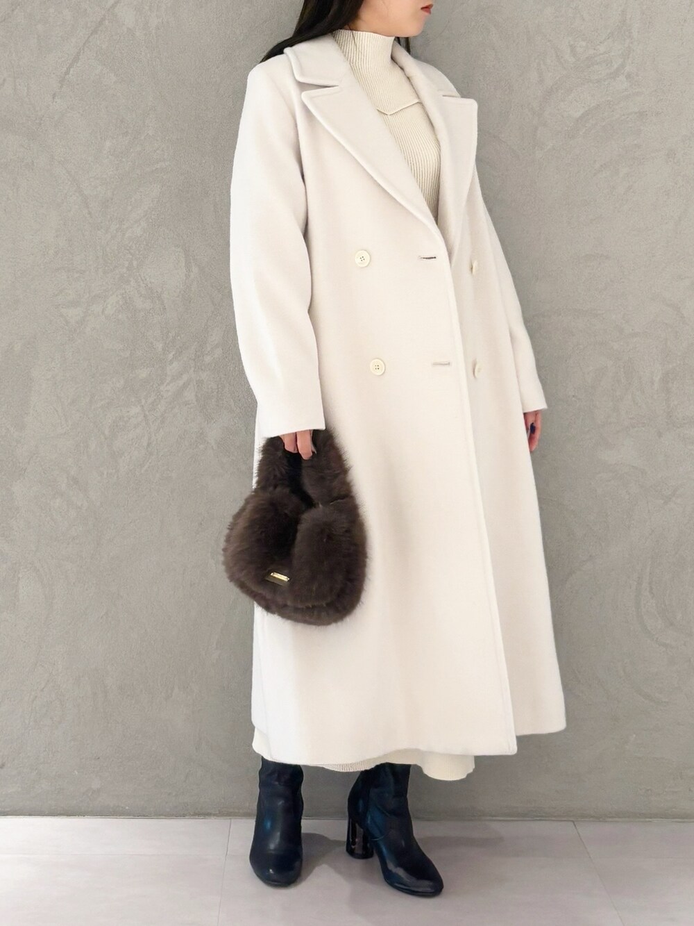 ホワイト系のチェスターコート、ブラック系のブーツ、ブラウン系のハンドバッグを着用したレディースの冬コーディネートの3枚目の写真