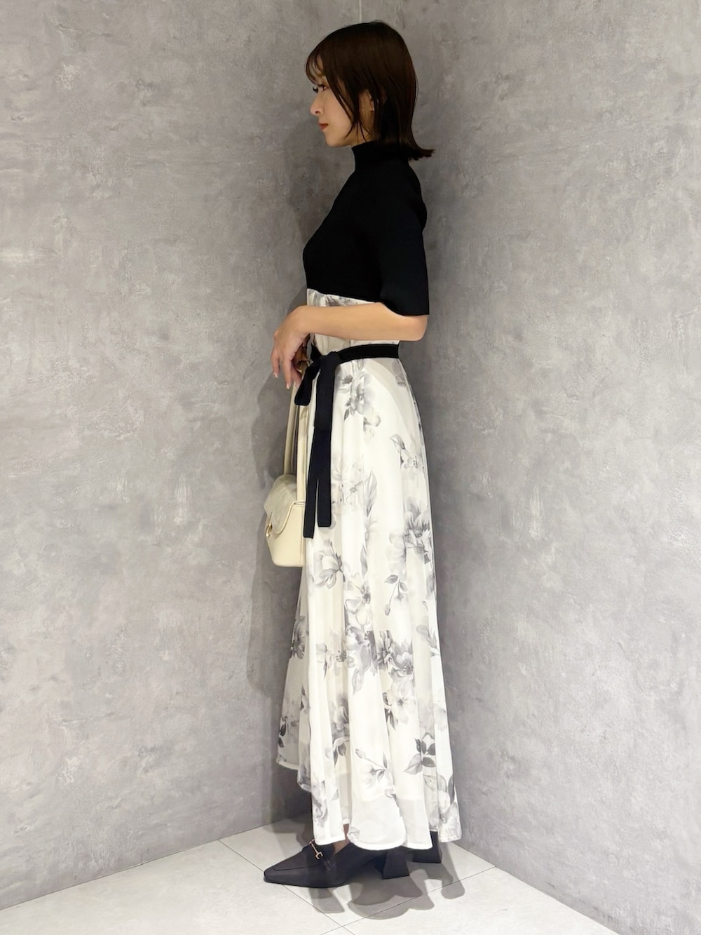 ブラック系のワンピース、ブラウン系のパンプス、ホワイト系のハンドバッグを着用したレディースの春コーディネートの2枚目の写真