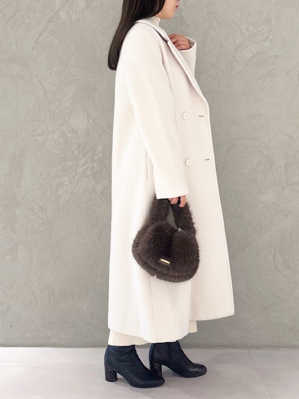 ホワイト系のチェスターコート、ブラック系のブーツ、ブラウン系のハンドバッグを着用したレディースの冬コーディネートの2枚目の写真