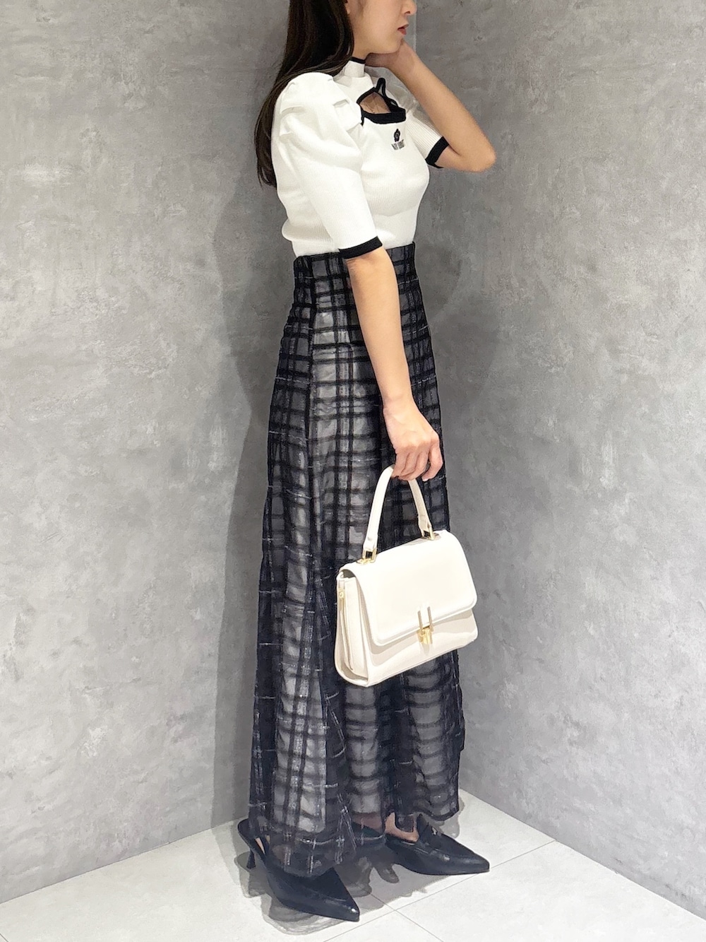 ブルー系のスカート、ブラック系のパンプス、ホワイト系のハンドバッグを着用したレディースの春コーディネートの4枚目の写真