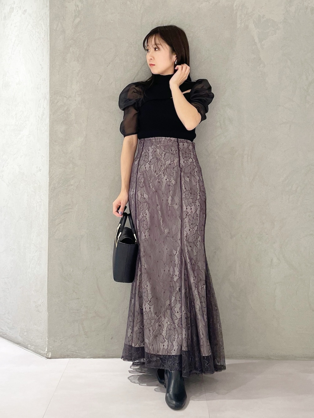 パープル系のスカート、ブラック系のハンドバッグ、ブラック系のニット/セーターを着用したレディースの春コーディネートの5枚目の写真