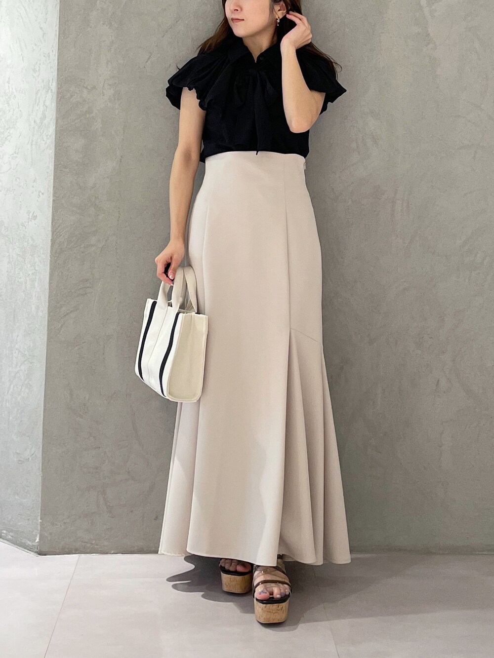 グレー系のハンドバッグ、ベージュ系のスカート、ブラック系のサンダルを着用したレディースの春コーディネートの4枚目の写真