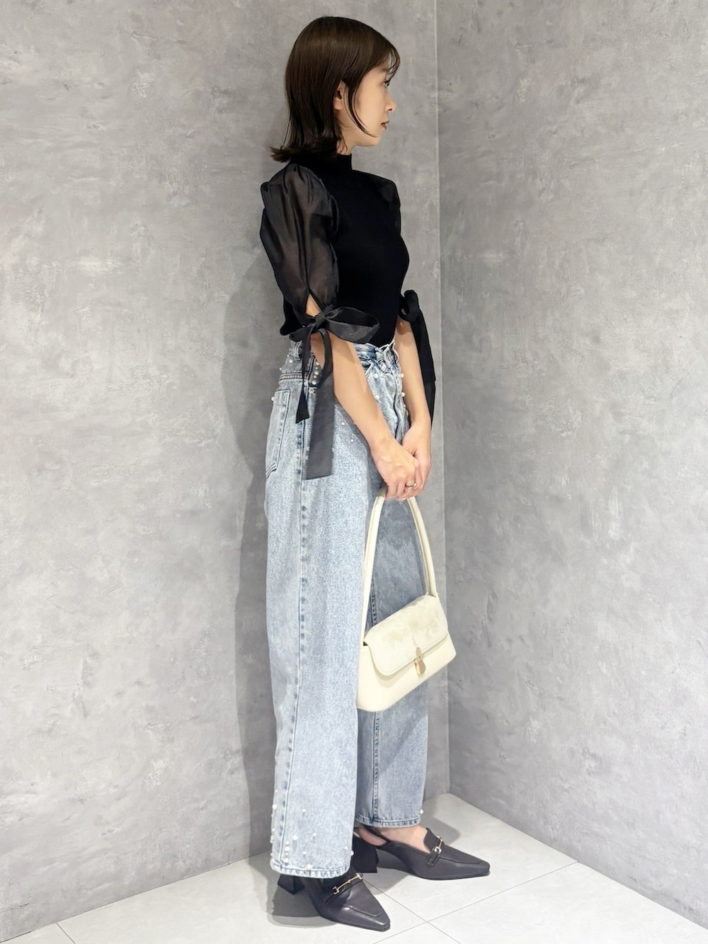 ブルー系のデニムパンツ、ブラック系のニット/セーター、ホワイト系のハンドバッグを着用したレディースの春コーディネートの2枚目の写真