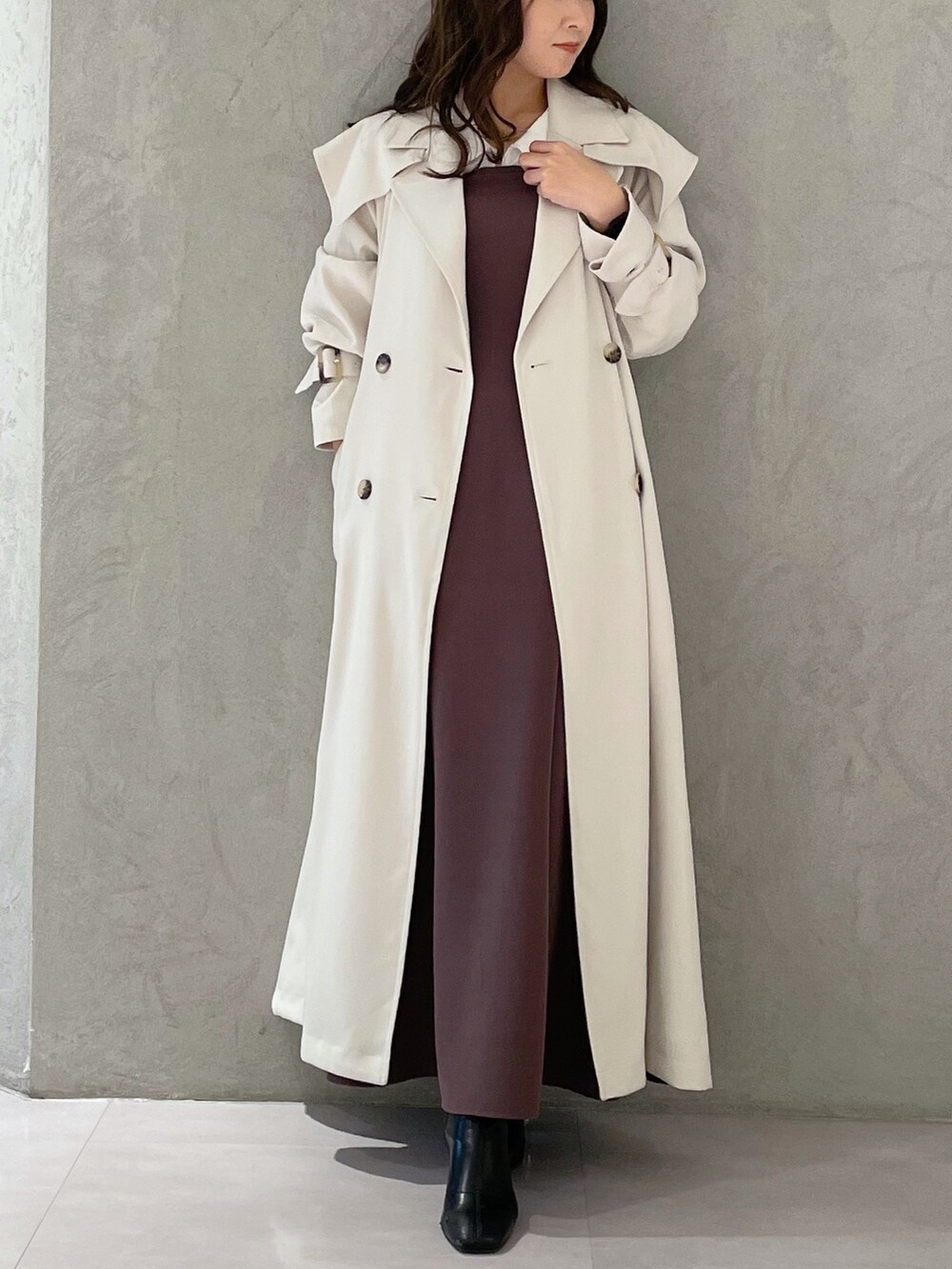 パープル系のワンピース、ブラック系のブーツ、ホワイト系のトレンチコートを着用したレディースの冬コーディネートの7枚目の写真