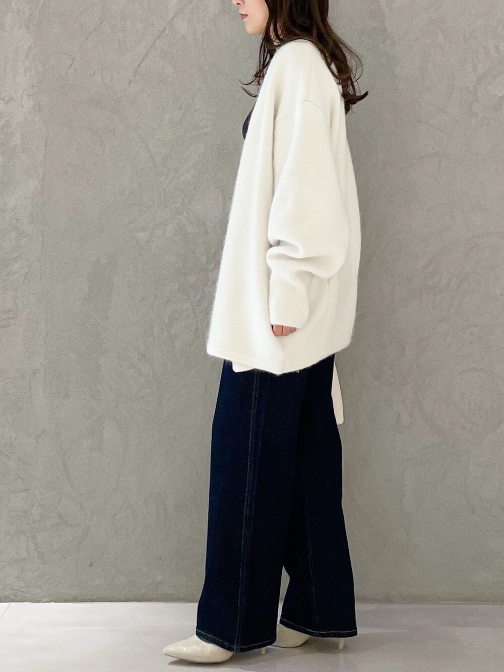 ブルー系のデニムパンツ、ホワイト系のハンドバッグ、ホワイト系のパンプスを着用したレディースの秋コーディネートの4枚目の写真