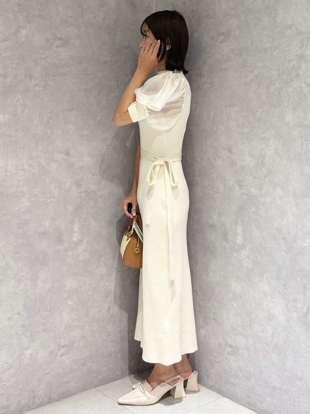 ホワイト系のワンピース、ホワイト系のパンプス、ブラウン系のハンドバッグを着用したレディースの春コーディネートの3枚目の写真
