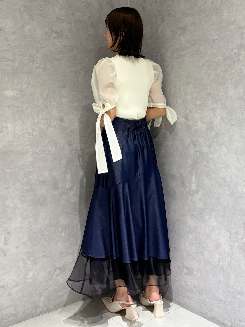 ブルー系のスカート、ホワイト系のニット/セーター、ホワイト系のパンプスを着用したレディースの春コーディネートの2枚目の写真