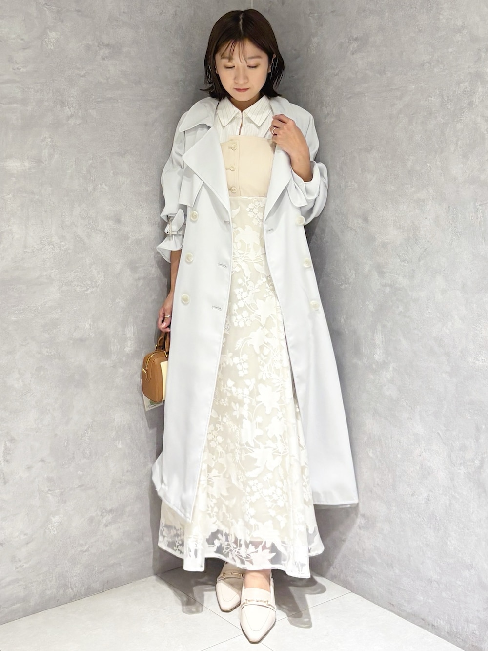 ブルー系のトレンチコート、ベージュ系のワンピース、ブラウン系のハンドバッグを着用したレディースの春コーディネートの4枚目の写真