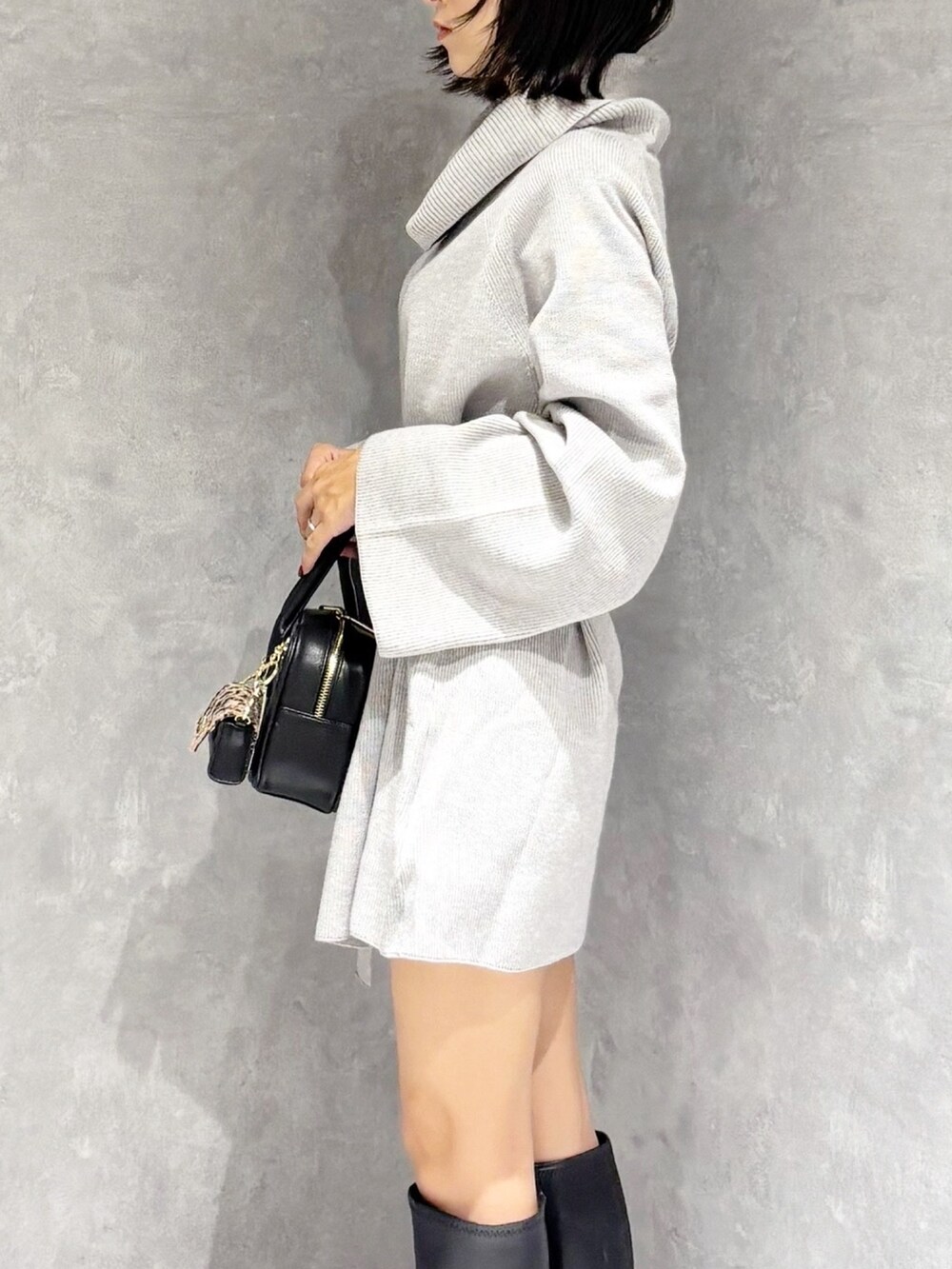 グレー系のニット/セーター、ブラック系のブーツ、ブラック系のハンドバッグを着用したレディースの秋コーディネートの4枚目の写真