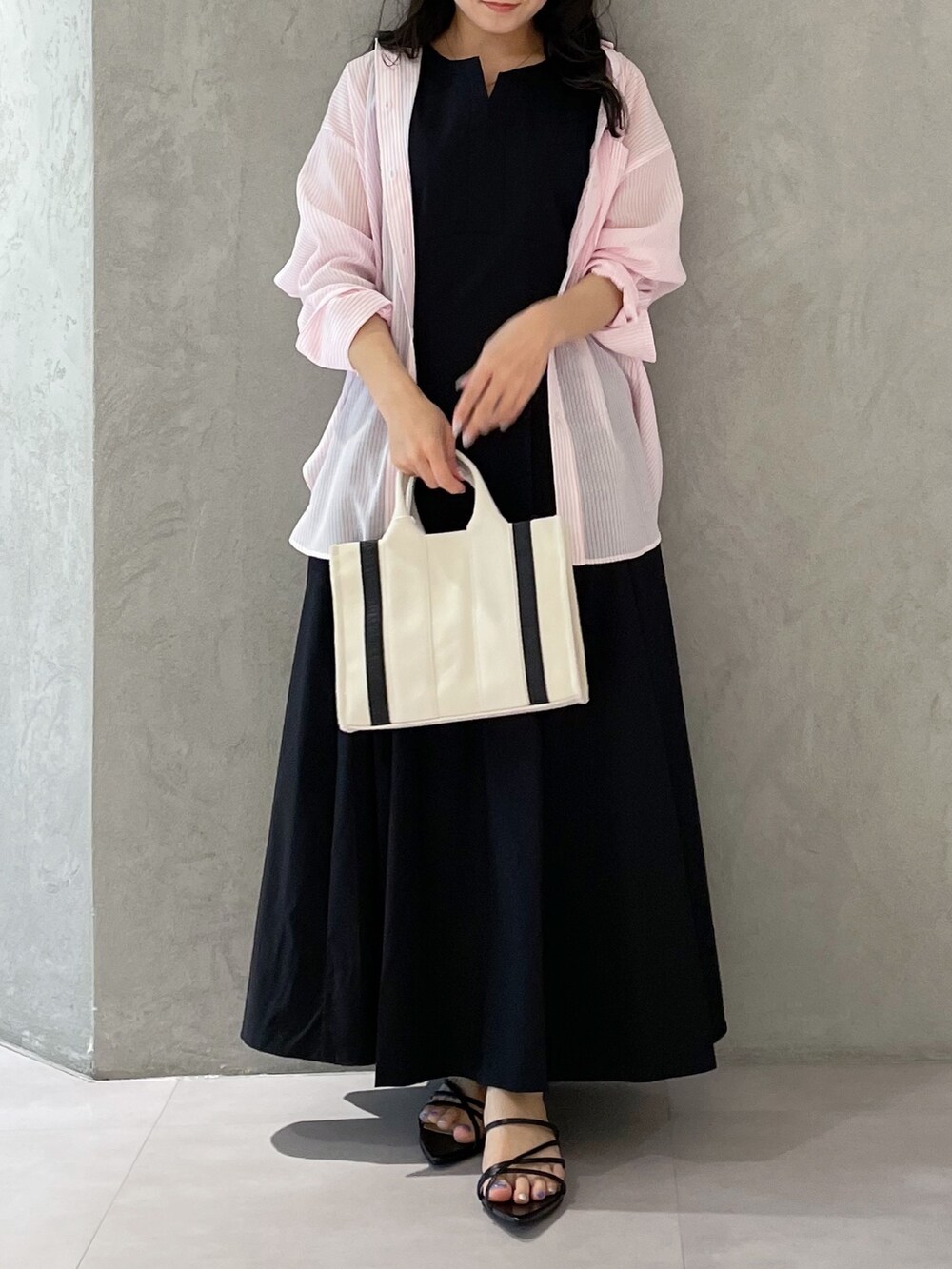 ブラック系のワンピース、ブラック系のサンダル、ホワイト系のハンドバッグを着用したレディースの春コーディネートの3枚目の写真