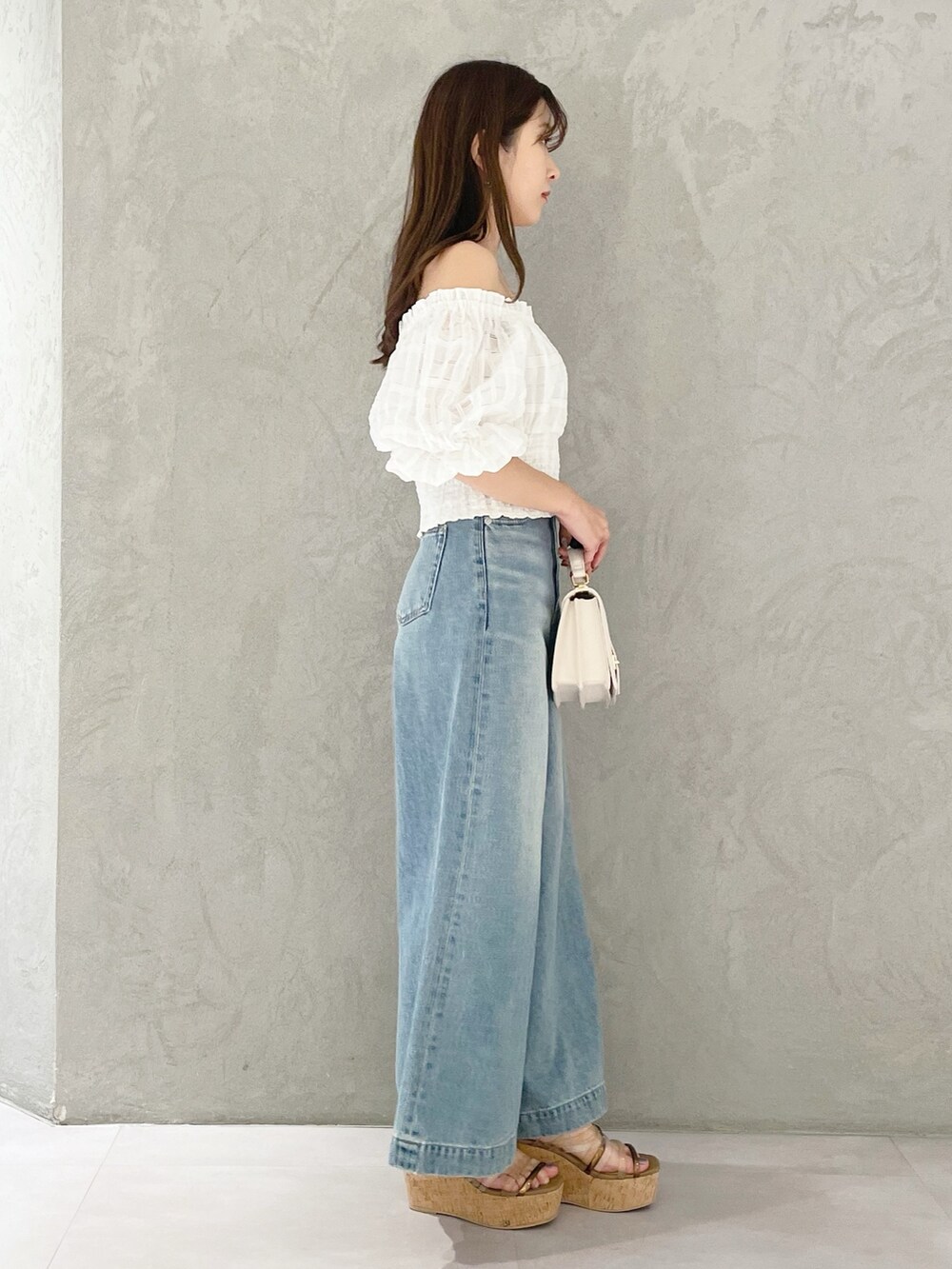 ブルー系のデニムパンツ、ブラウン系のサンダル、ホワイト系のハンドバッグを着用したレディースの春コーディネートの3枚目の写真