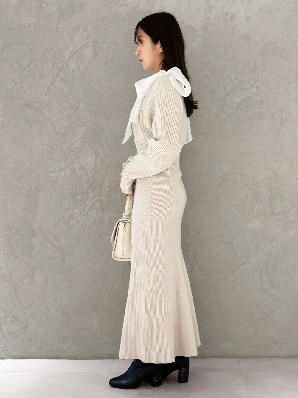 ホワイト系のハンドバッグ、ブラック系のブーツ、ホワイト系のワンピースを着用したレディースの冬コーディネートの7枚目の写真