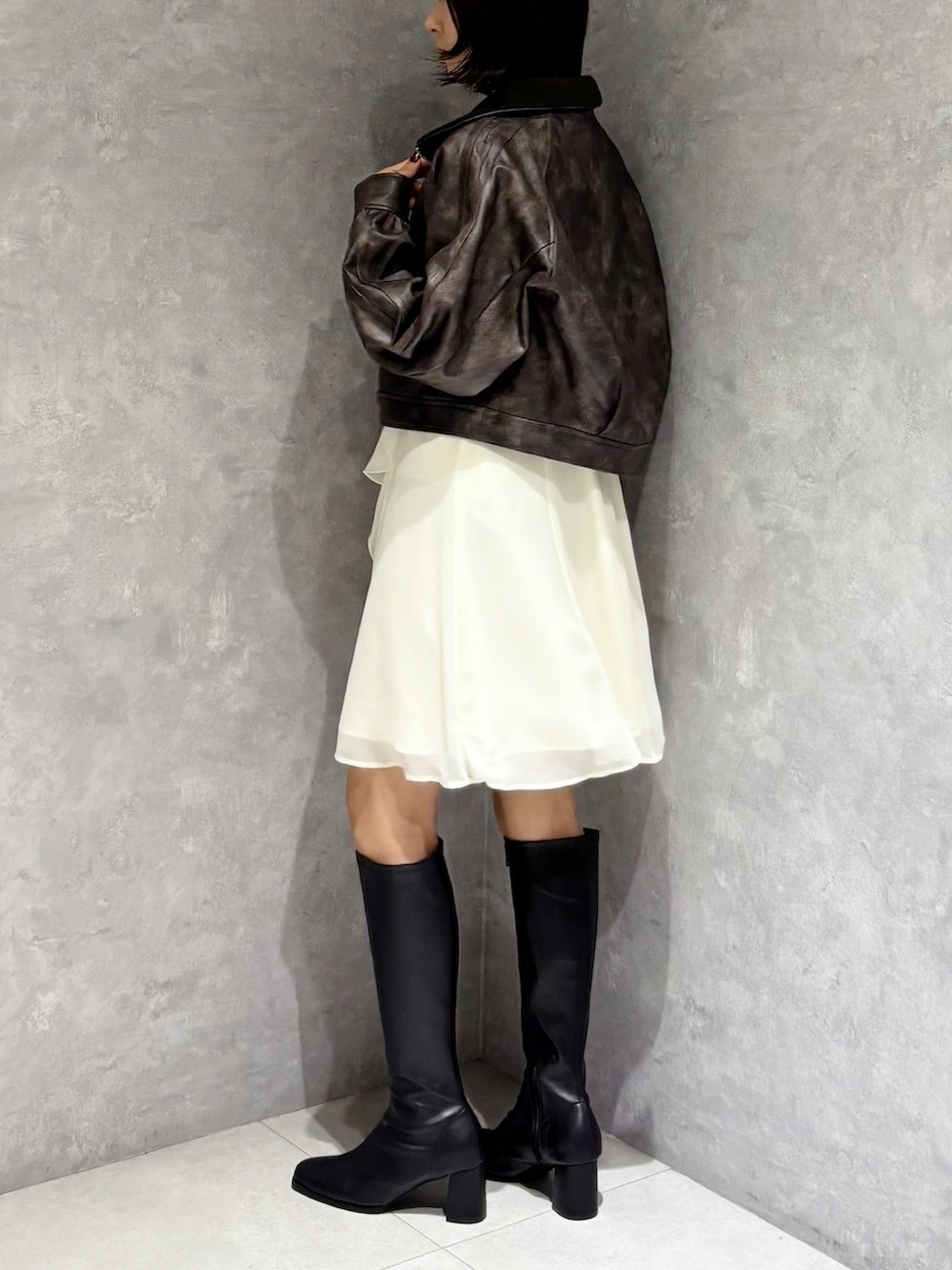 ブラック系のブーツ、ブラウン系のブルゾン、ホワイト系のワンピースを着用したレディースの秋コーディネートの3枚目の写真