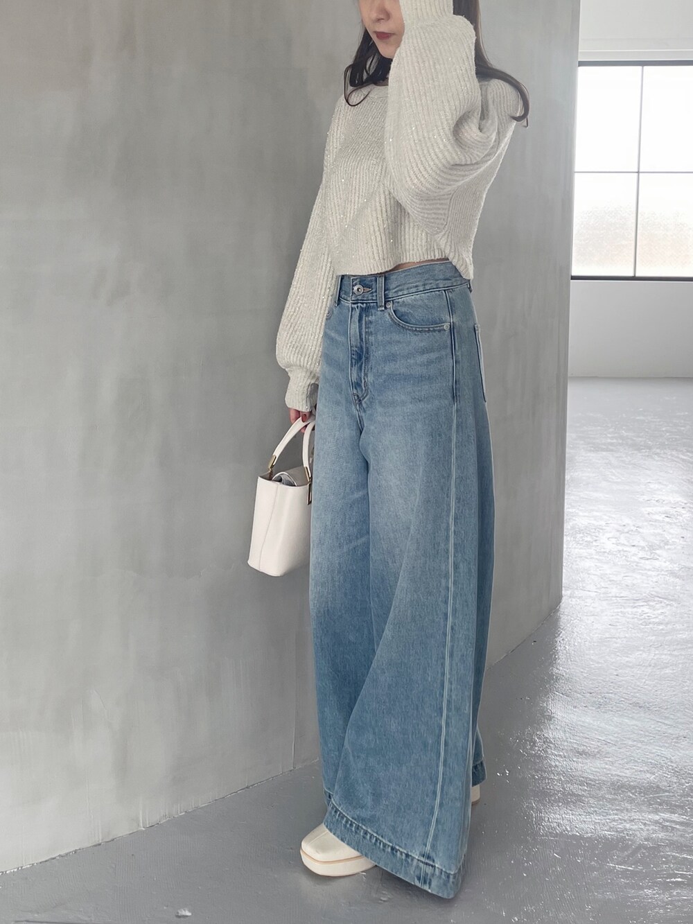ホワイト系のブーツ、ホワイト系のハンドバッグ、ブルー系のデニムパンツを着用したレディースの秋コーディネートの5枚目の写真