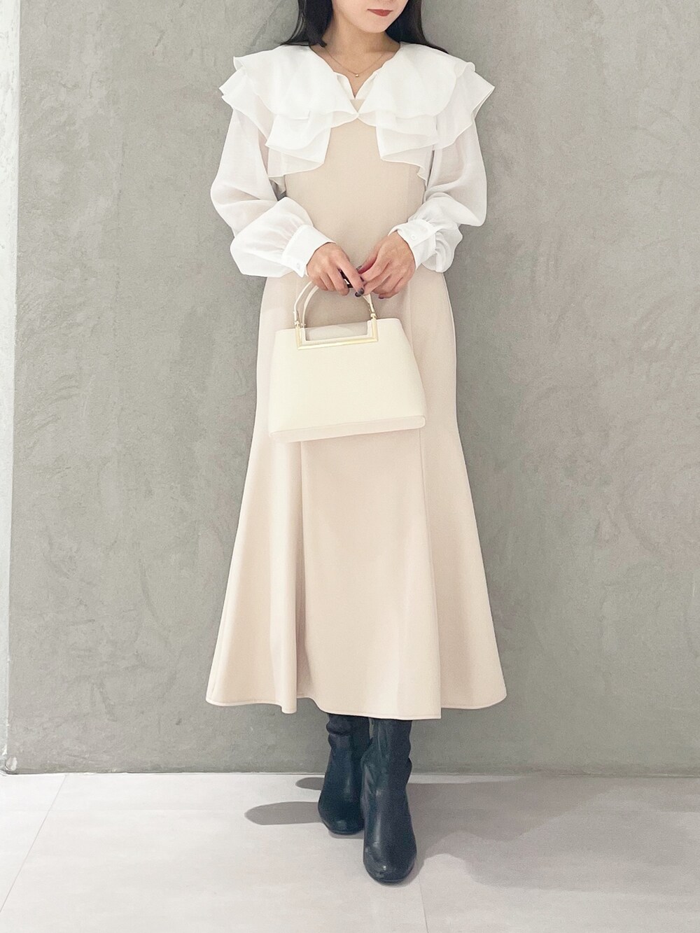 ベージュ系のワンピース、ホワイト系のハンドバッグ、ブラック系のブーツを着用したレディースの冬コーディネートの5枚目の写真