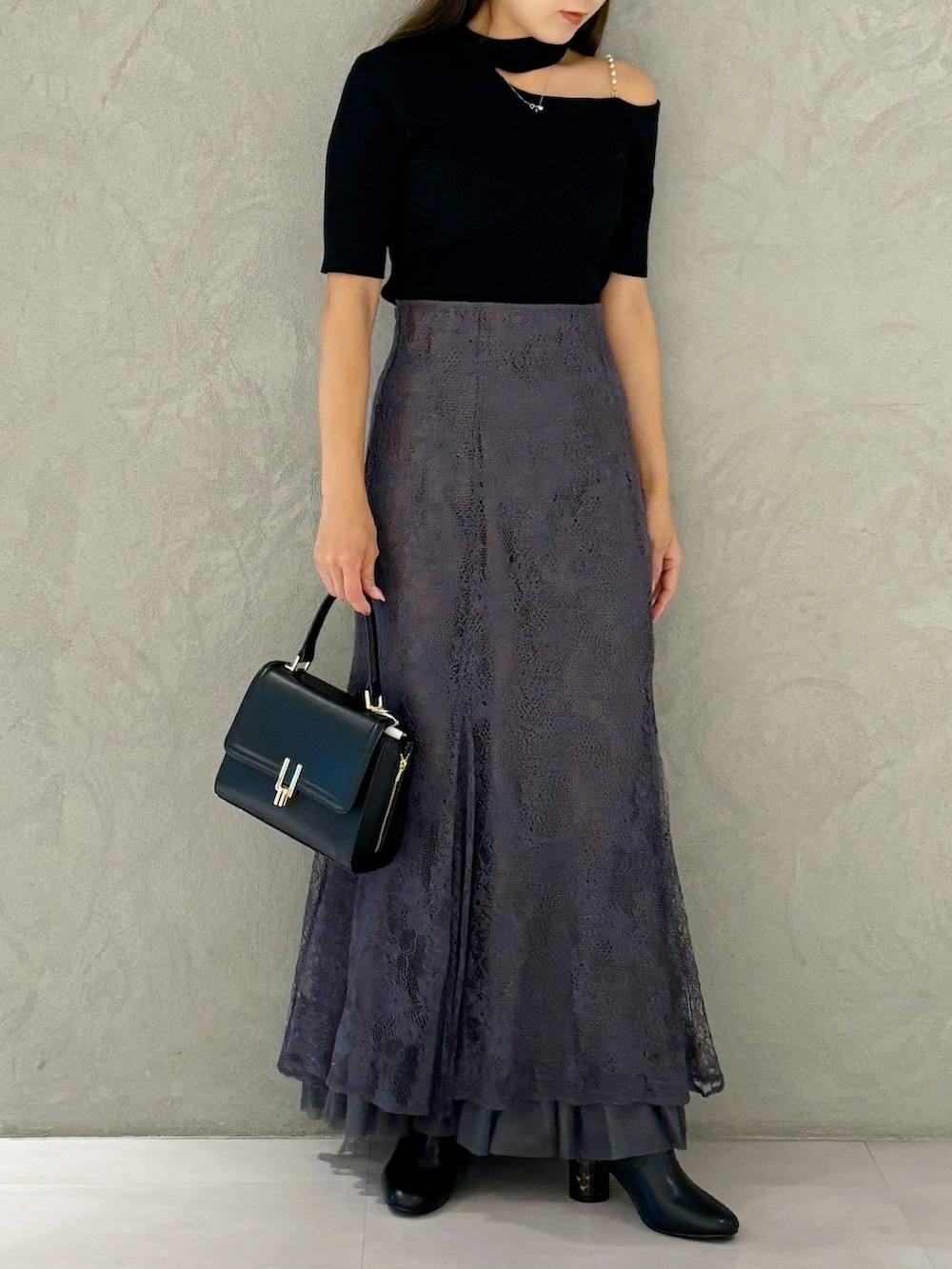 グレー系のスカート、ブラック系のブーツ、ブラック系のショルダーバッグを着用したレディースの秋コーディネートの2枚目の写真