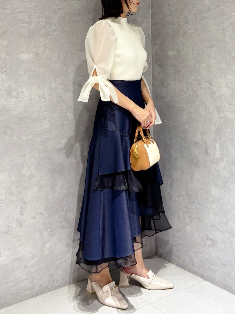 ブルー系のスカート、ホワイト系のニット/セーター、ホワイト系のパンプスを着用したレディースの春コーディネートの3枚目の写真