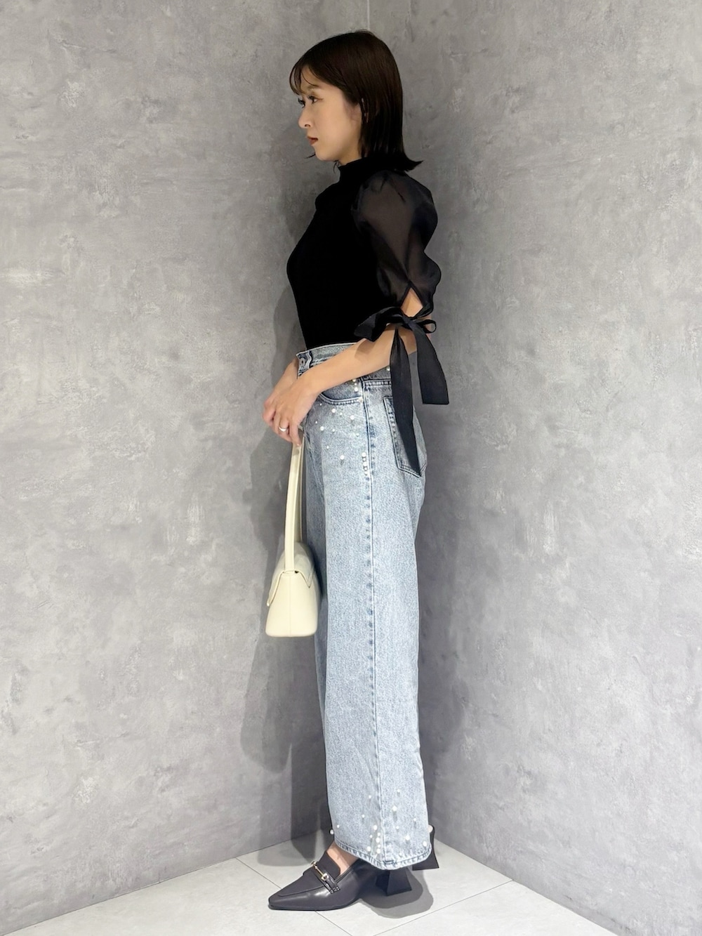 ブルー系のデニムパンツ、ブラック系のニット/セーター、ホワイト系のハンドバッグを着用したレディースの春コーディネートの4枚目の写真