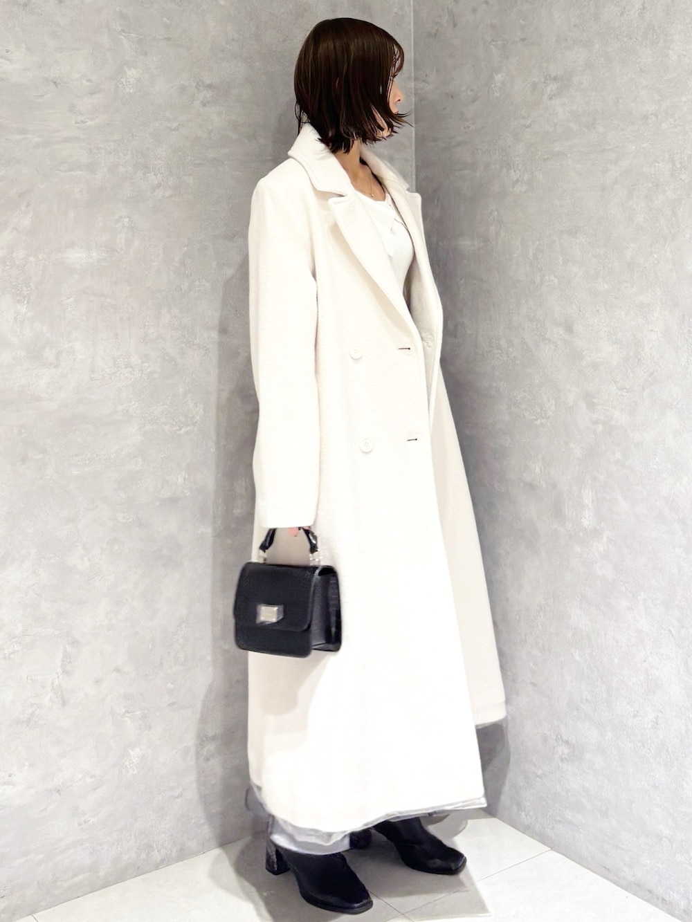 ホワイト系のチェスターコート、ブラック系のブーツ、ホワイト系のニット/セーターを着用したレディースの冬コーディネートの2枚目の写真
