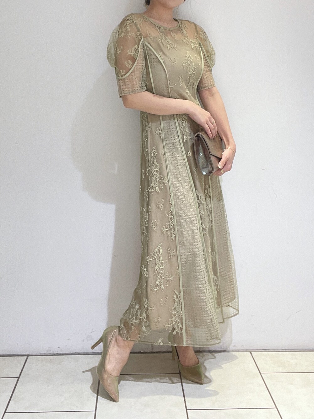 ゴールド系のハンドバッグ、グリーン系のドレス、ゴールド系のパンプスを着用したレディースの冬コーディネートの4枚目の写真