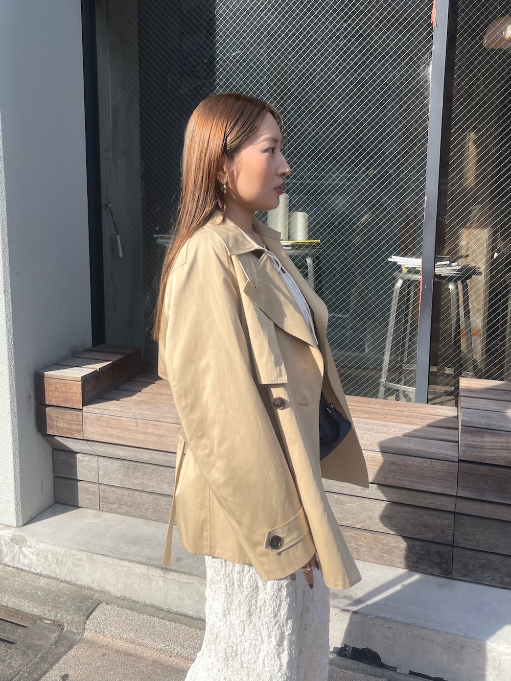 ホワイト系のワンピース、ベージュ系のトレンチコート、ゴールド系のピアス（両耳用）を着用したレディースの冬コーディネートの5枚目の写真