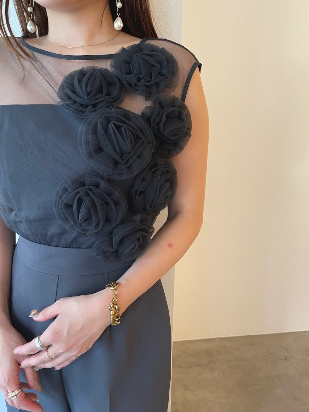 シルバー系のパンプス、グレー系のパンツドレス、ゴールド系のピアス（両耳用）を着用したレディースの夏コーディネートの6枚目の写真