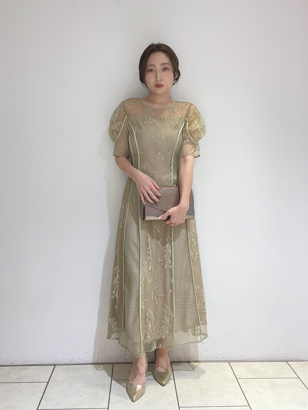 ゴールド系のハンドバッグ、グリーン系のドレス、ゴールド系のパンプスを着用したレディースの冬コーディネートの6枚目の写真