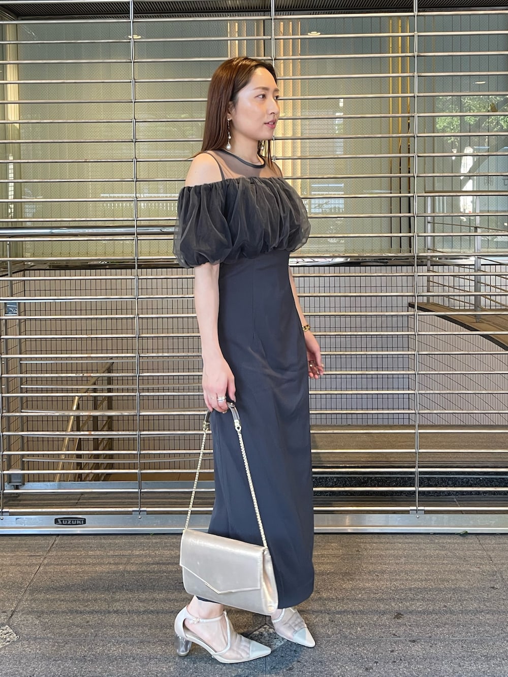 グレー系のドレス、ゴールド系のクラッチバッグ、ゴールド系のピアス（両耳用）を着用したレディースの夏コーディネートの4枚目の写真