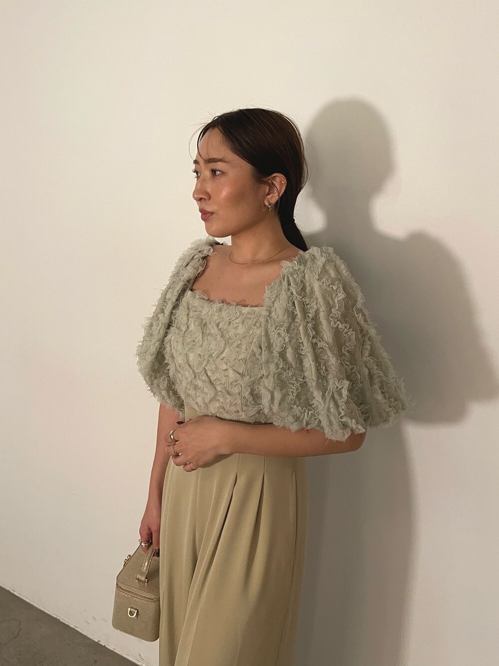 ゴールド系のハンドバッグ、ゴールド系のパンプス、グリーン系のパンツドレスを着用したレディースの冬コーディネートの9枚目の写真
