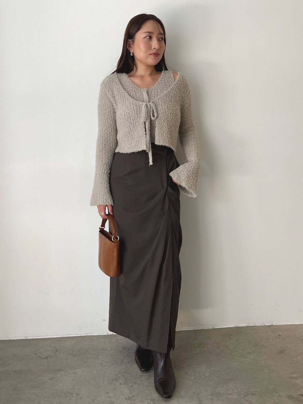 グレー系のアンサンブル、イエロー系のハンドバッグ、ブラウン系のスカートを着用したレディースの秋コーディネートの2枚目の写真